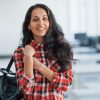 In casual clothes. Portrait of attractive young woman standing in the office with black bag.
